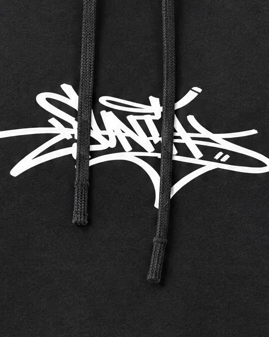 Acercamiento a la firma de graffiti en blanco sobre la sudadera negra.